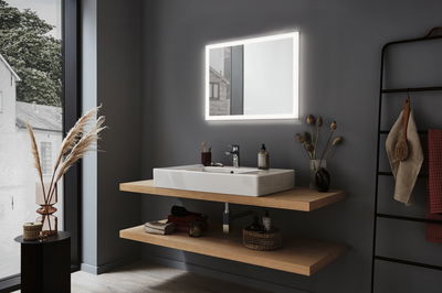 Moderne badkamer met verlichte rechthoekige spiegel en witte keramische wastafel op houten planken