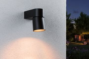 Black metal outdoor wall light with warm white illumination on white wall in garden at night