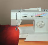 White Singer sewing machine with red fabric on wooden table, mechanical controls and stitch pattern display
