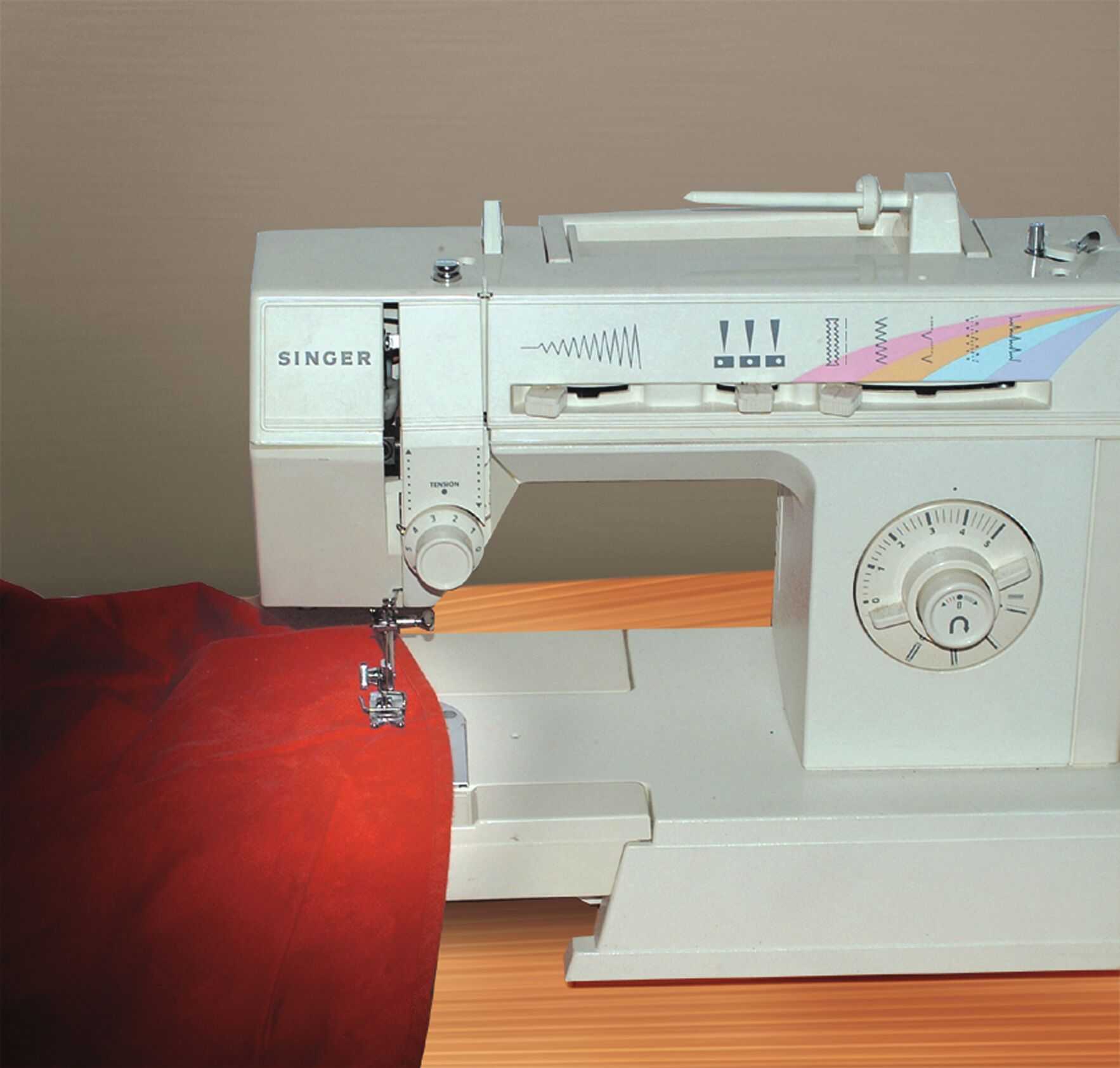 White Singer sewing machine with red fabric on wooden table, mechanical controls and stitch pattern display