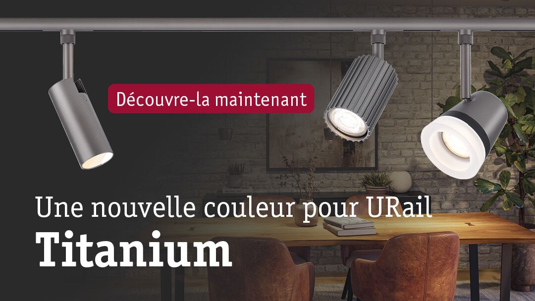 Trois spots LED URail en métal couleur titane au-dessus d'une table en bois dans un salon moderne avec mur en briques