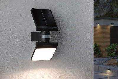 Schwarze Solar-Außenwandleuchte mit Bewegungsmelder an grauer Wand, moderne LED-Gartenbeleuchtung