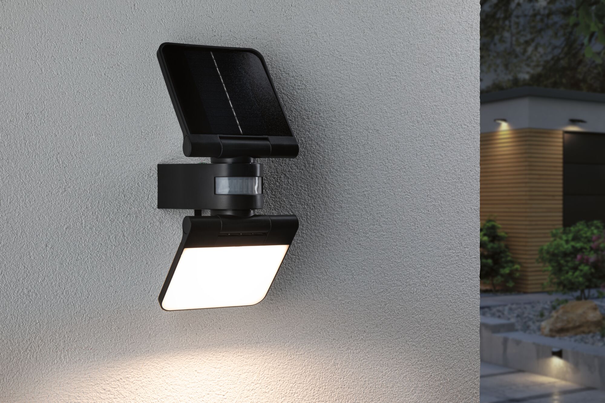 Black solar outdoor wall light with motion sensor on grey wall, modern LED garden lighting