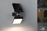 Black solar outdoor wall light with motion sensor on grey wall, modern LED garden lighting