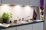 Plan de travail de cuisine moderne avec évier en acier inoxydable, pots d'herbes et éclairage LED sous meuble