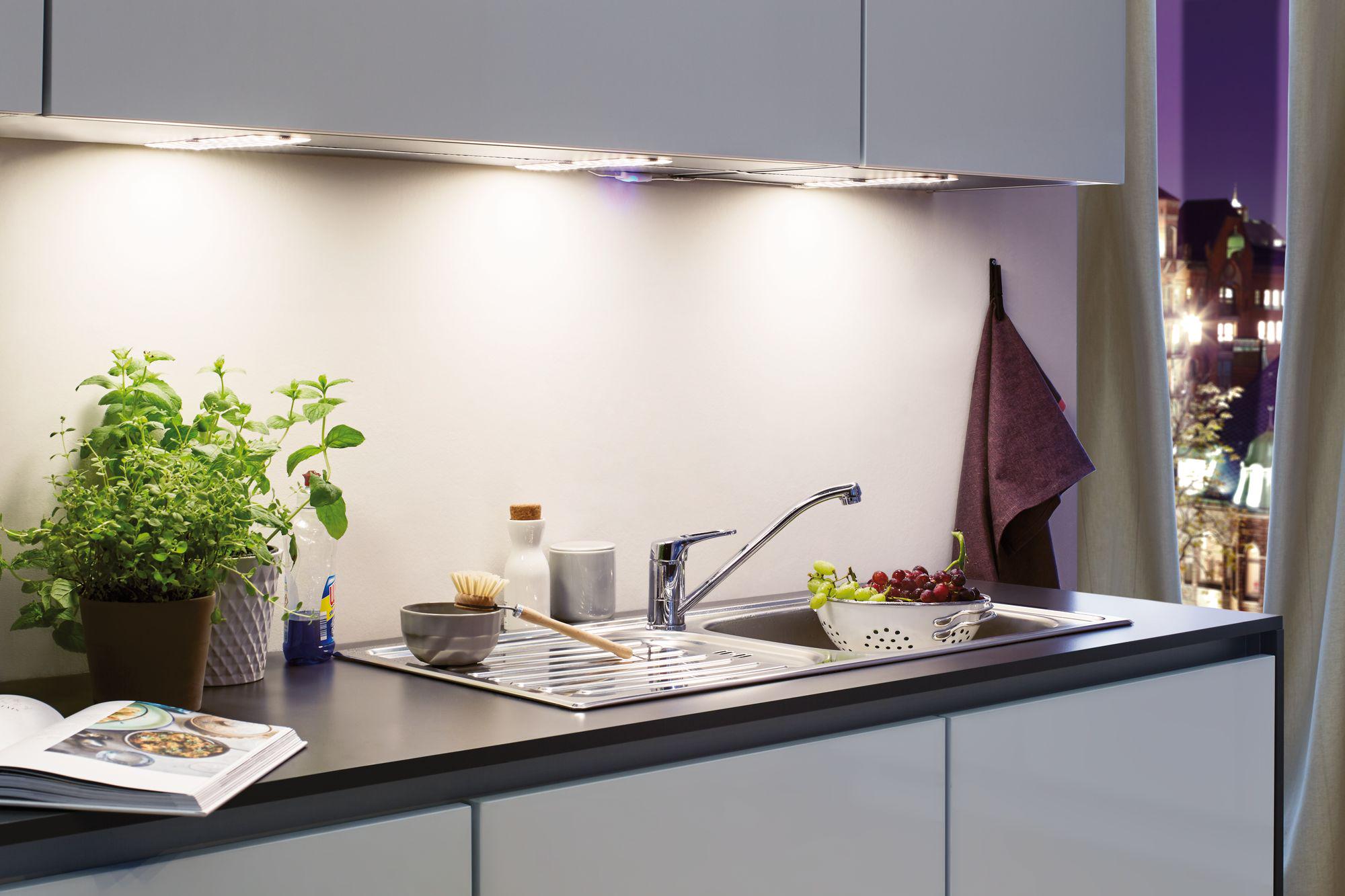 Plan de travail de cuisine moderne avec évier en acier inoxydable, pots d'herbes et éclairage LED sous meuble