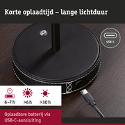 Zwarte ronde oplaadbasis met USB-C aansluiting en witte stiksels op donker houten tafel