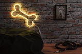Yellow LED bone-shaped wall lamp made of plastic on brick wall with dog leash nearby.