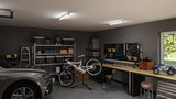 Moderne Werkstatt mit LED-Deckenleuchten, Fahrrad auf Ständer, Werkzeugwand und Werkbank mit Stauraum.
