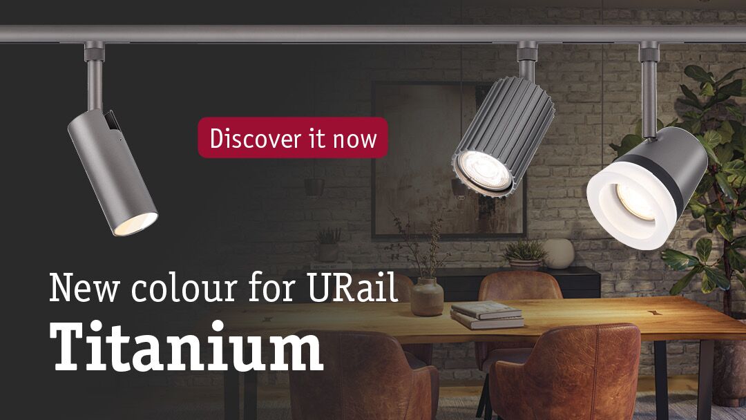 Three titanium-coloured URail metal LED spotlights above wooden table in modern dining room with brick wall.
