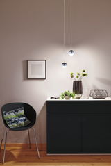 Moderne Pendelleuchten mit runden schwarzen Metallkugeln über schwarzem Sideboard in Wohnraum.