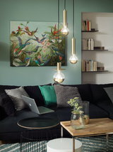 Salon moderne avec canapé en cuir noir, coussins verts et suspensions dorées pour éclairage intérieur élégant
