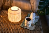 Ceramic light with delicate pattern glowing warmly on woven table with coffee cup and vase