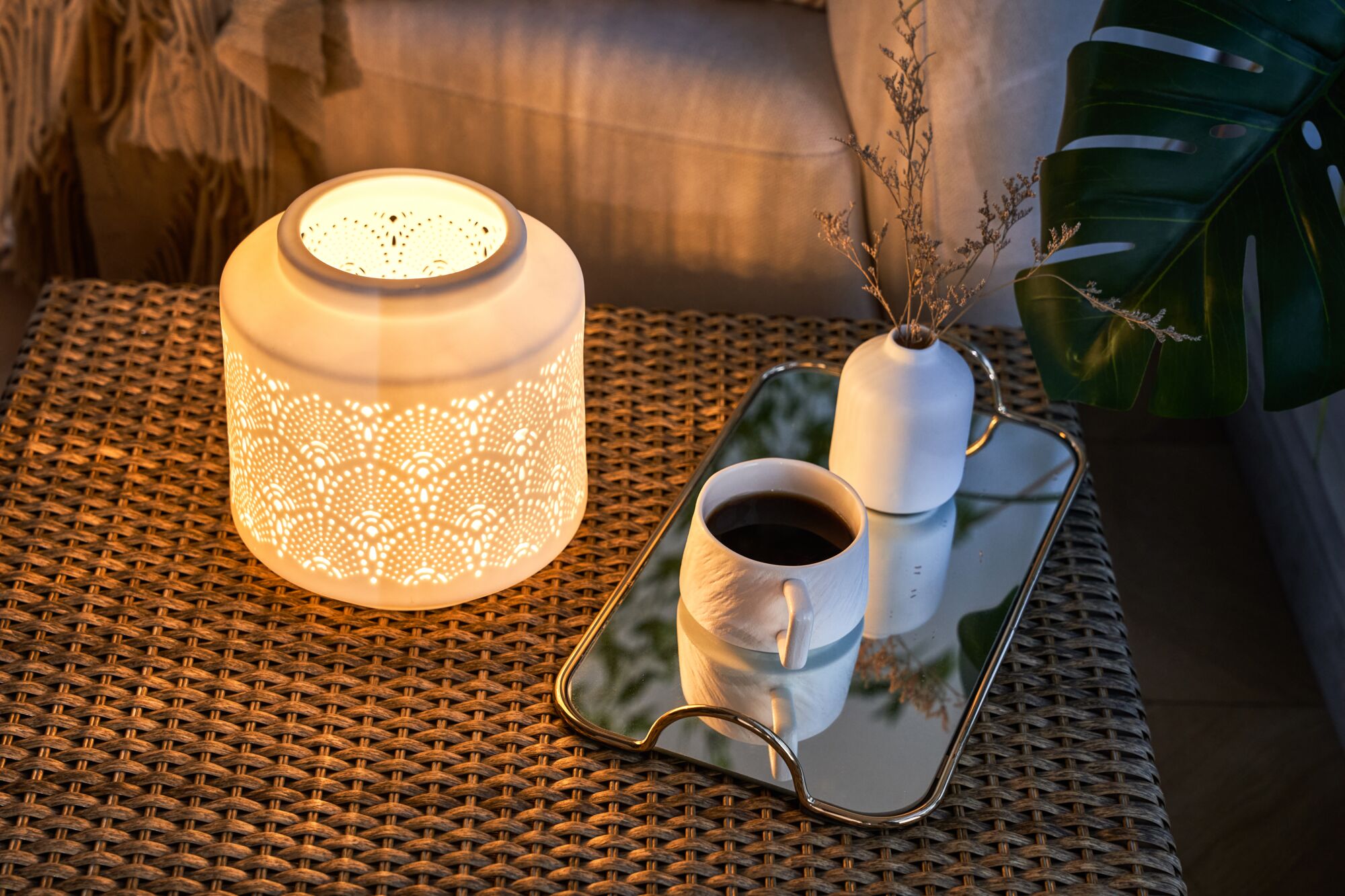 Keramik-Tischlampe mit filigranen Mustern in warmem Licht auf Rattantisch neben Kaffeetasse