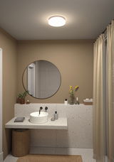 Round white ceiling light with warm white glow in modern bathroom with beige walls.