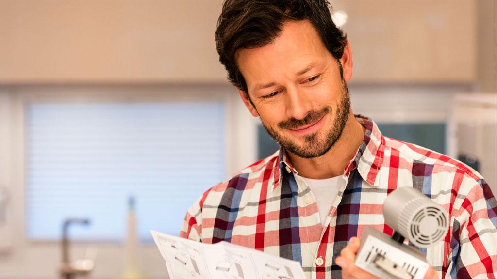 Mann liest Anleitung und hält weißen LED-Strahler in moderner Küche, Lichtmontage erklärt.