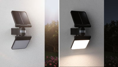 Schwarze Solar-LED-Wandleuchte mit Bewegungsmelder, tagsüber und nachts an einer weißen Wand montiert