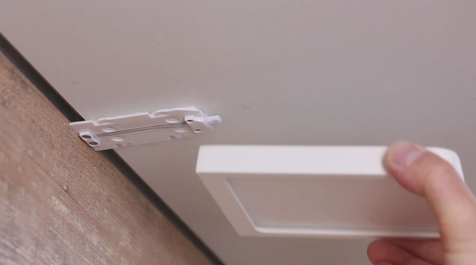 Hand holding white square LED panel frame near plastic ceiling mount for LED lights installation