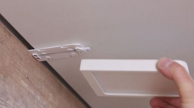 Hand hält weißen quadratischen LED-Panelrahmen nahe einer Deckenhalterung aus Kunststoff für LED-Leuchten