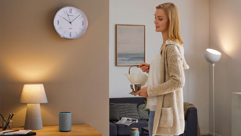 Frau gießt Tee in modernem Wohnzimmer mit grauer Tischlampe und Stehlampe, gemütliche Beleuchtung.