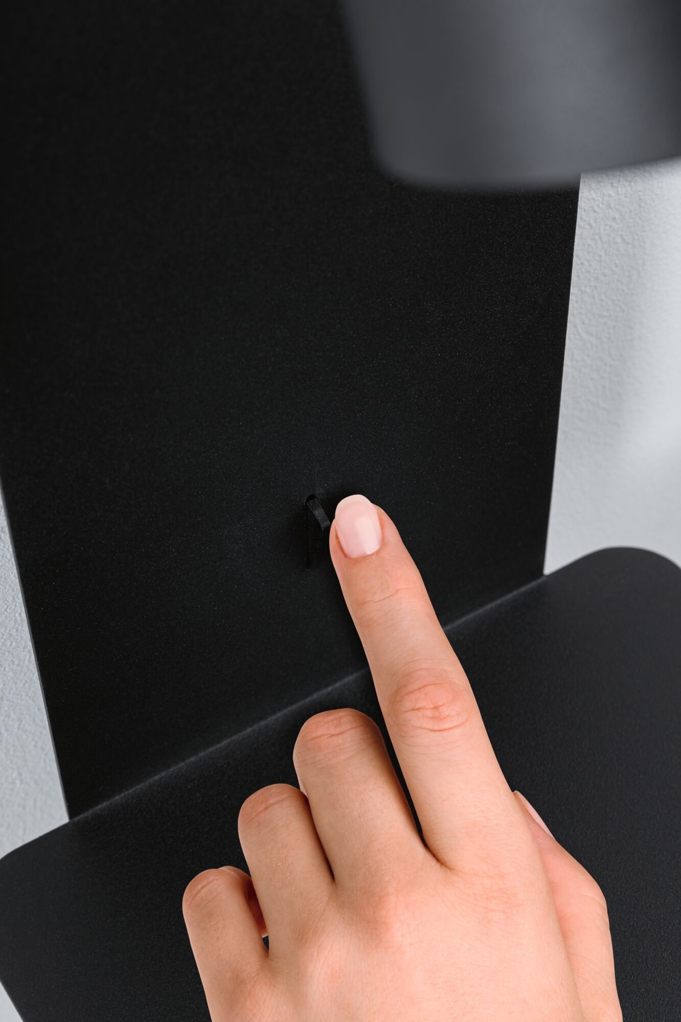 Main appuyant sur un petit interrupteur noir sur panneau métallique noir mat pour contrôle d'éclairage