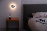 Moderne witte LED-wandlamp met leeslamp boven houten nachtkastje in slaapkamer.