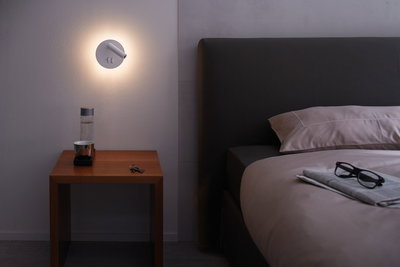 Moderner weißer LED-Wandleuchter mit Leselicht über Nachttisch aus Holz im Schlafzimmer.