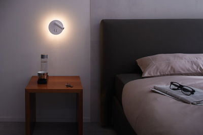 Modern white LED wall light with reading lamp above wooden bedside table in bedroom.