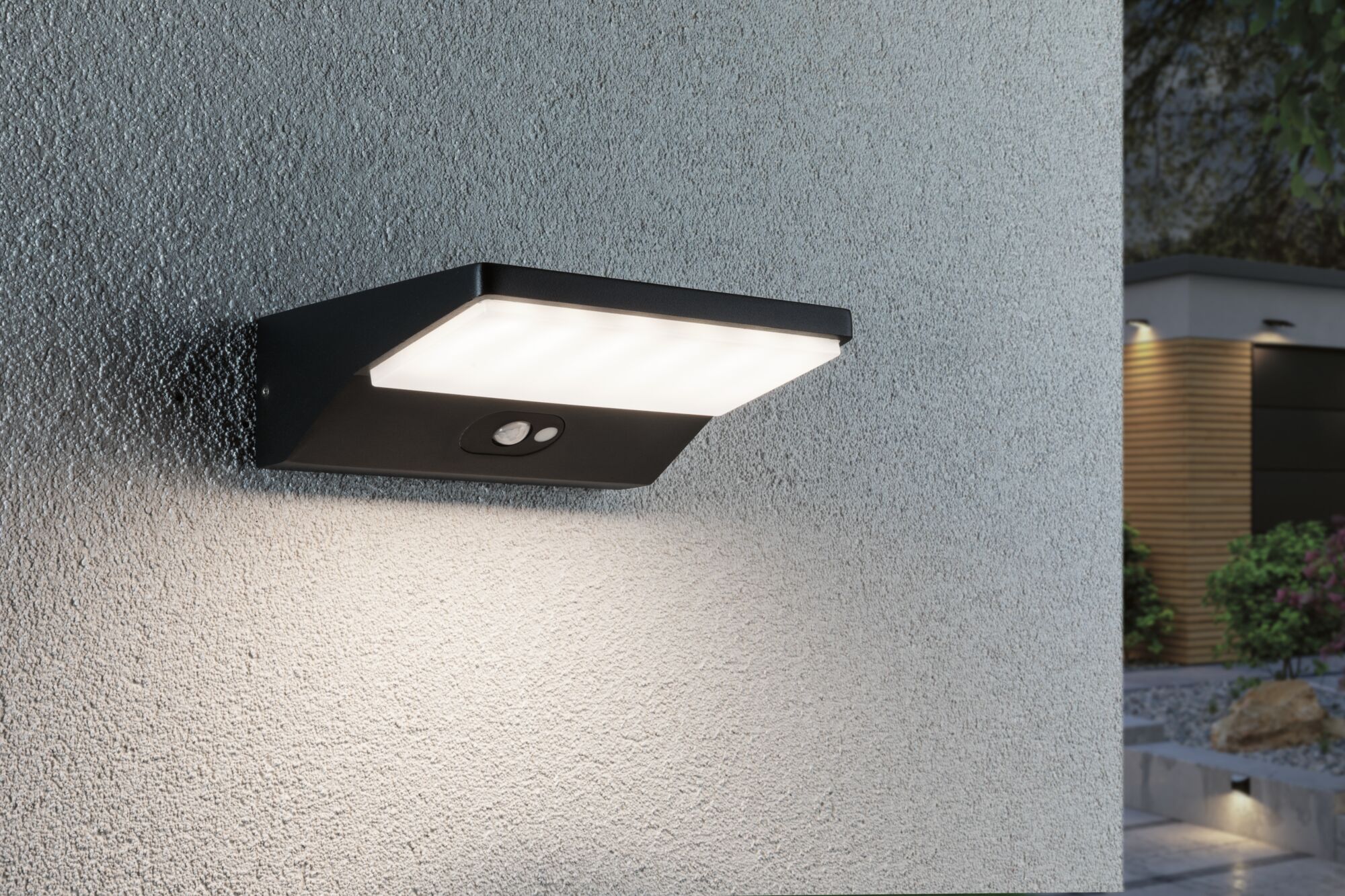 Schwarze LED-Außenwandleuchte aus Metall mit Bewegungsmelder an grauer Wand für Gartenbeleuchtung