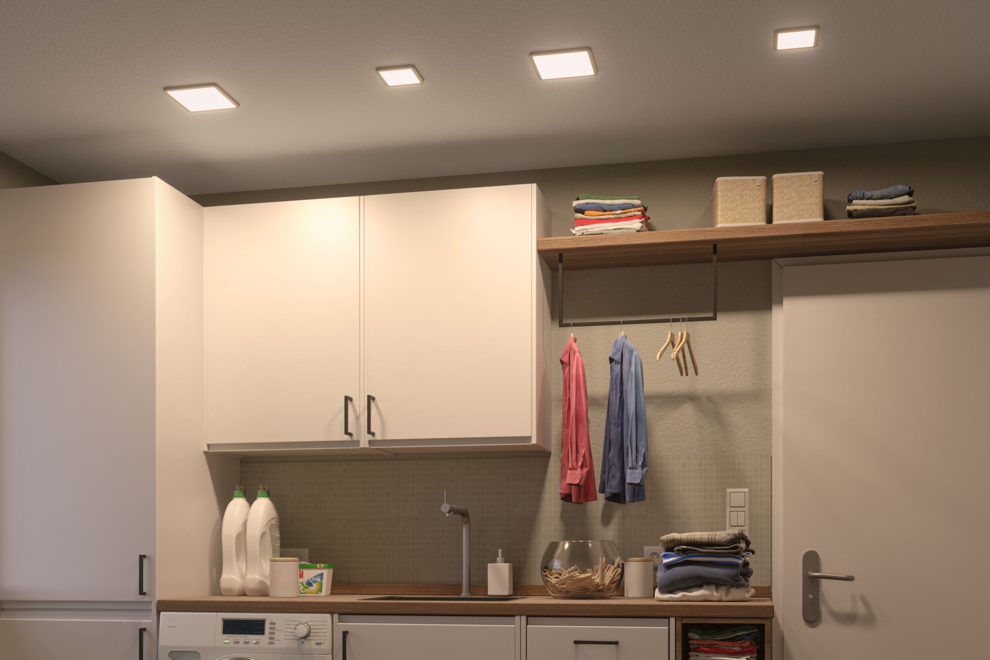 Modern white square recessed lights illuminate bright laundry room with wooden countertop and storage.