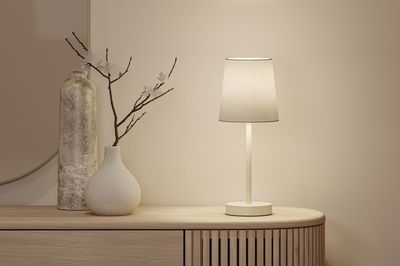 Beige tafellamp met stoffen kap op houten dressoir naast twee decoratieve vazen in neutrale kleuren