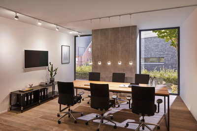 Moderne vergaderruimte met houten tafel, zwarte bureaustoelen en Paulmann VariLine LED-plafondspots.