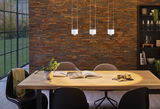 Drie witte LED-hanglampen boven lichte houten tafel met boeken en kopje in eetkamer met bakstenen muur