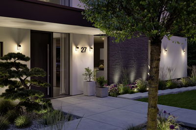 Éclairage extérieur moderne avec appliques murales blanc chaud sur maison blanche et chemin de jardin.