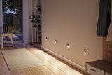 Vier moderne zilveren LED-wandlampen aan beige muur met houten vloer en vloerkleed in hal.