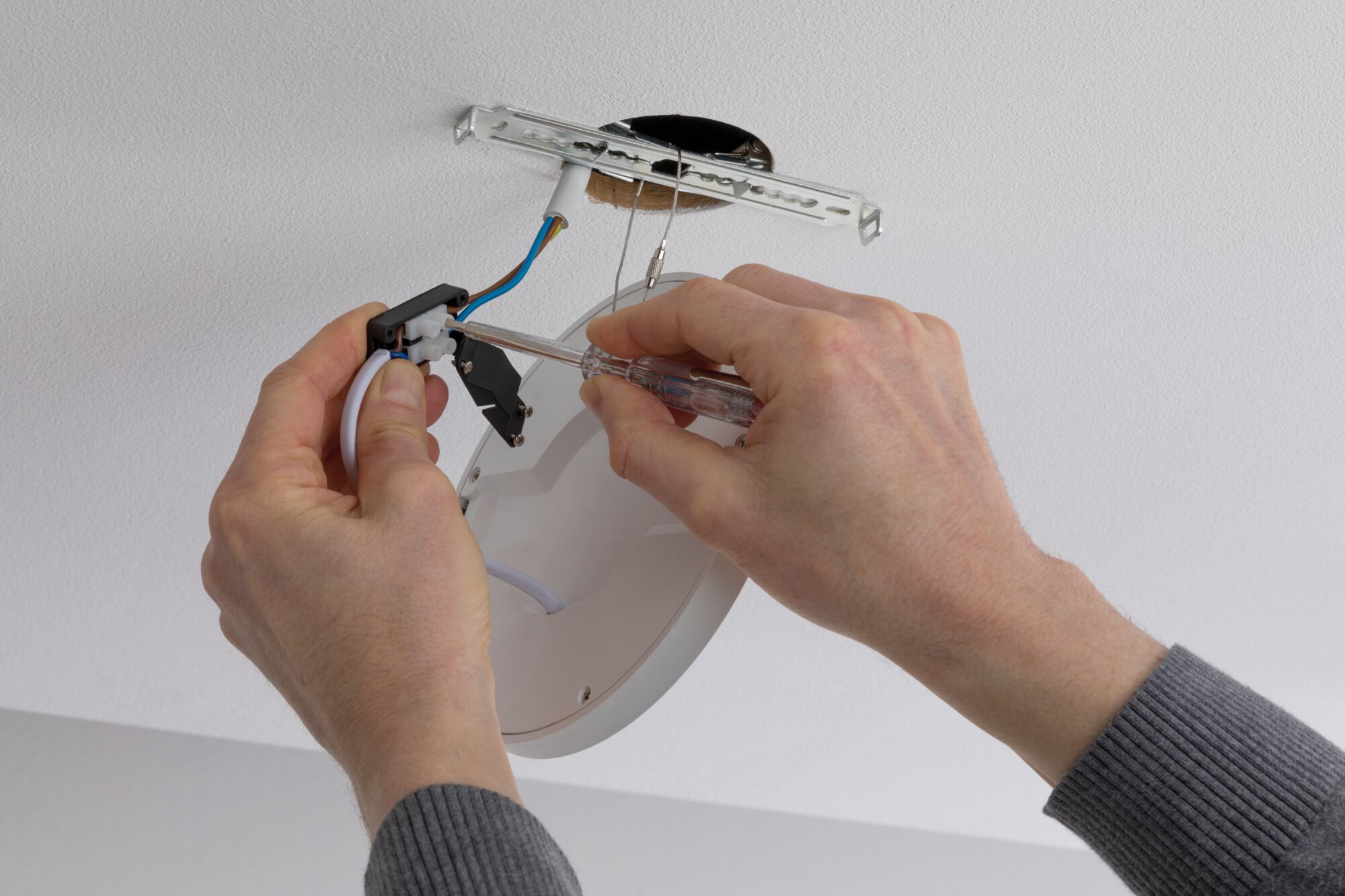 Installing white LED ceiling light with screwdriver on ceiling showing electrical wiring.