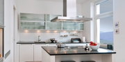 Modern white kitchen with black countertop and stainless steel extractor hood, kitchen lighting included