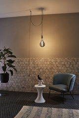 Modern living area with hanging LED bulb, blue armchair and white side table on black hexagon tile floor