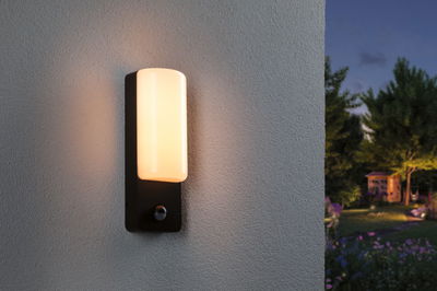 Modern black outdoor wall light with warm white glow and motion sensor for garden lighting.