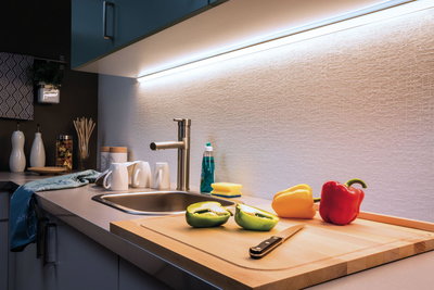 Modern kitchen countertop with stainless steel sink, wooden cutting board, and white LED under-cabinet lighting.