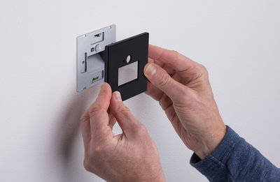 Montage einer schwarzen Abdeckplatte aus Kunststoff an einer Wandhalterung für Lichtschalter.