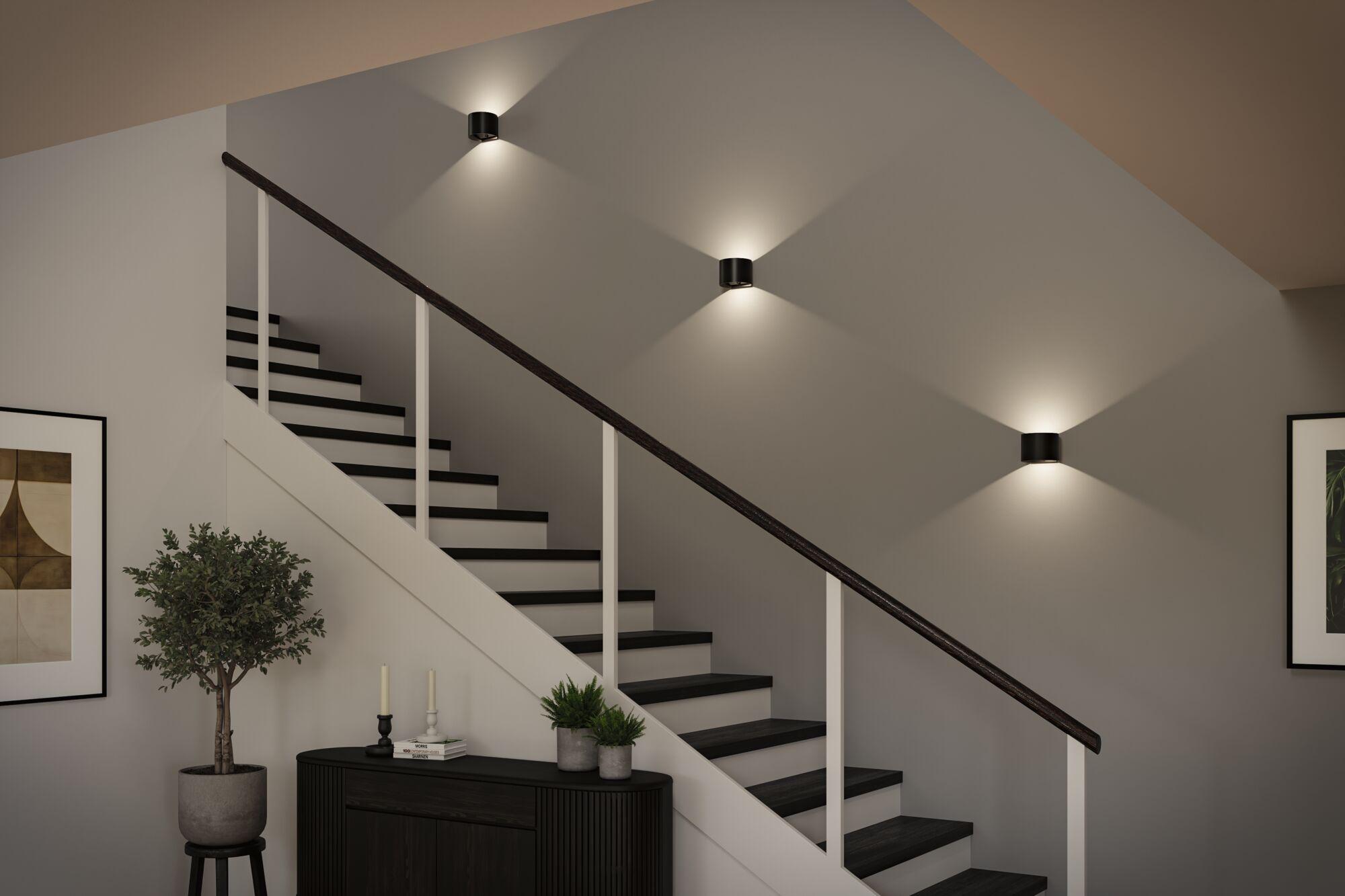 Schwarze LED-Stehleuchte mit zwei runden Leuchtringen neben beige Sofa im modernen Wohnzimmer mit Bücherregal.