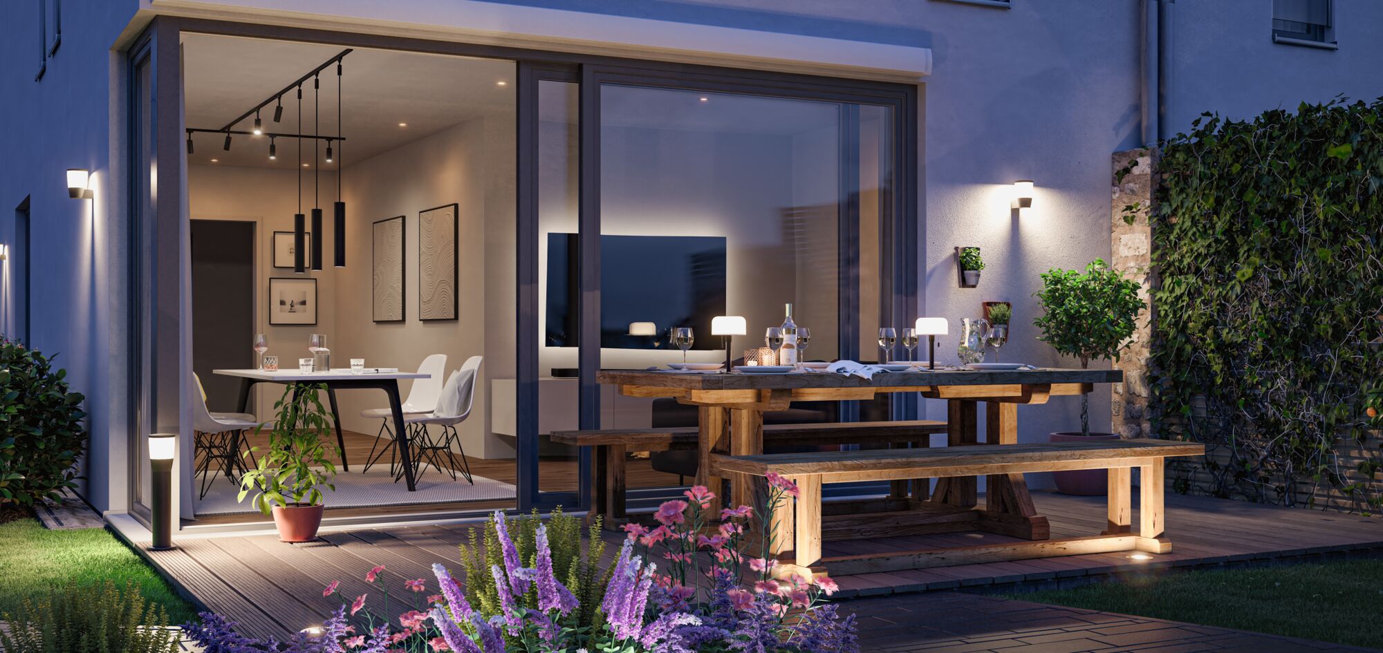 Abendliche Terrasse mit Holzbank und Tisch, moderner Außenbeleuchtung und blühenden Pflanzen