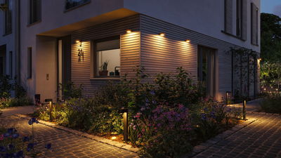 Éclairage extérieur moderne avec lumière blanche chaude sur façade de maison et chemin en pierre.
