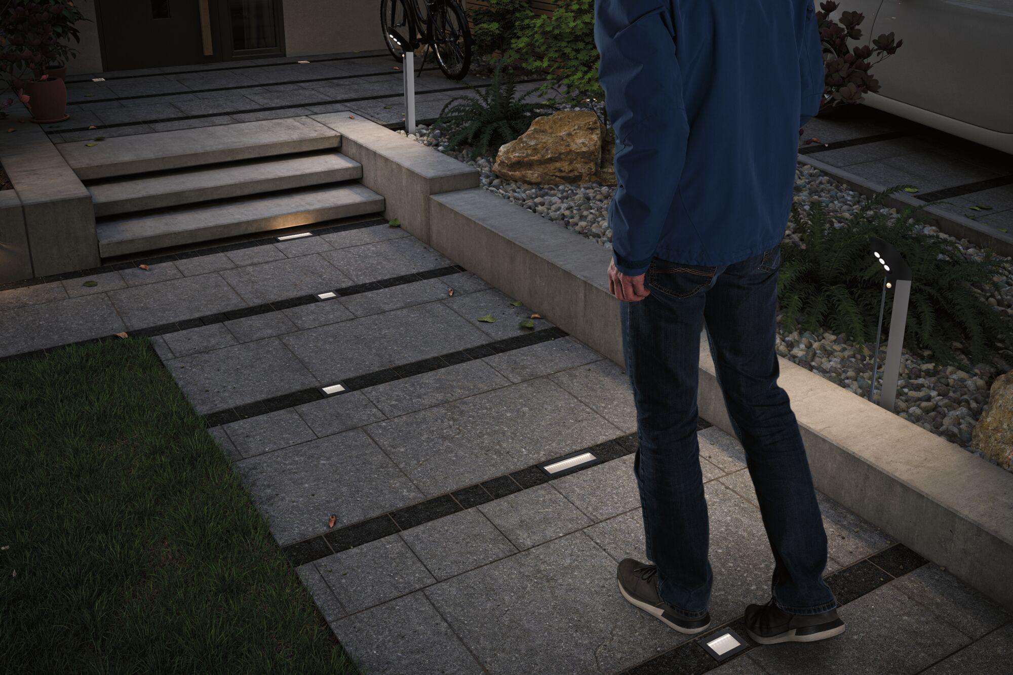 Modern outdoor lighting with recessed LED floor lights and standing lamps on grey stone pathway