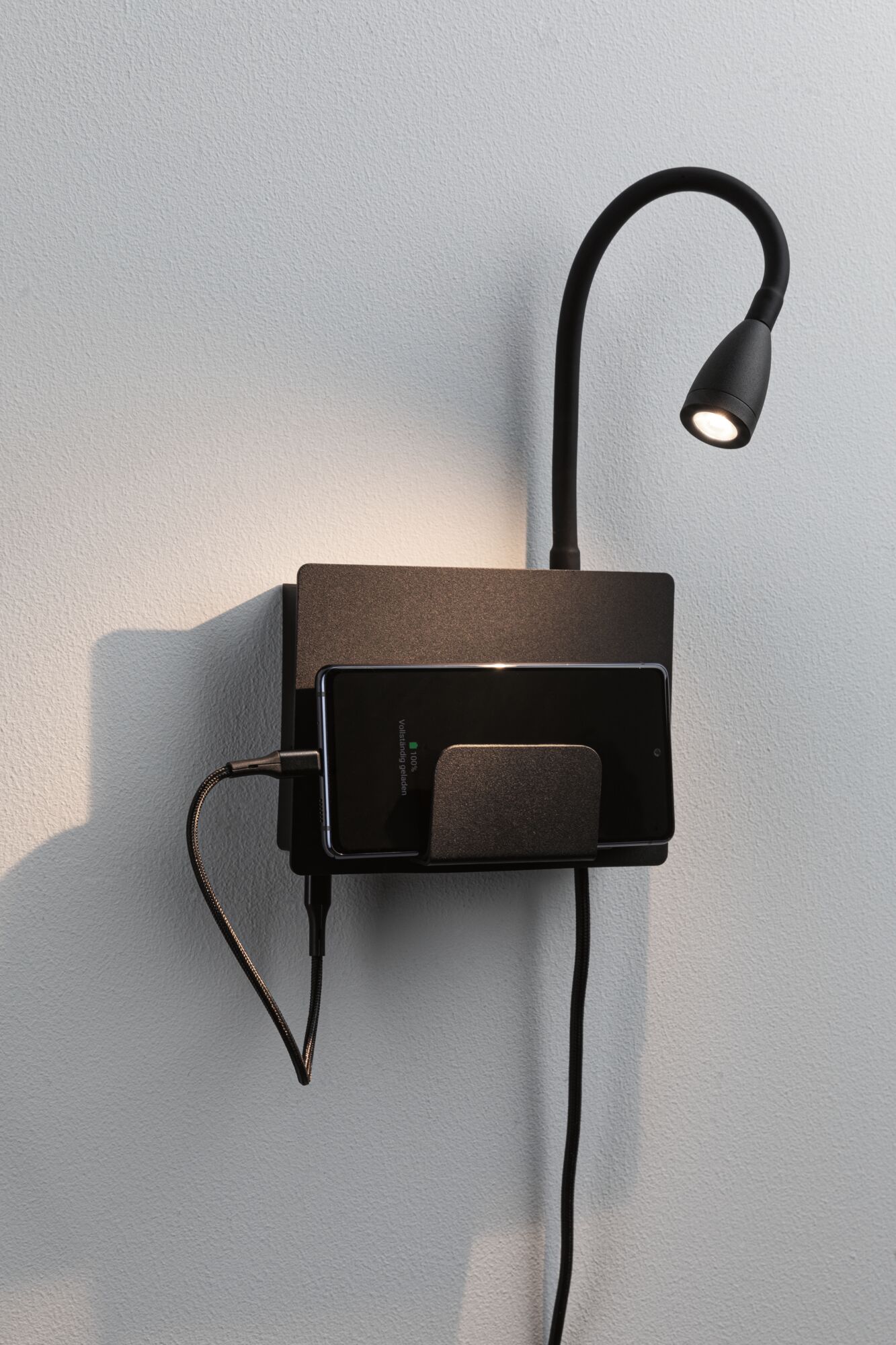 Black wall lamp with flexible reading arm and metal smartphone holder for modern charging and lighting