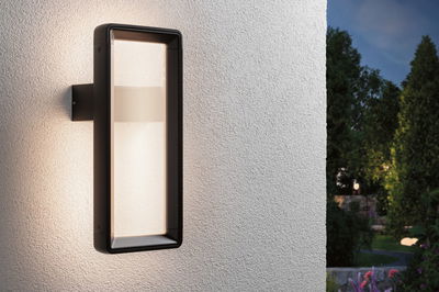 Rectangular black outdoor wall light in metal with warm white illumination on white wall in garden