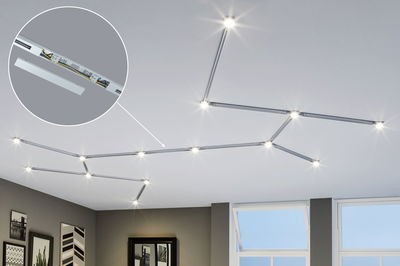 Modular silver LED track lighting with warm white light on white ceiling in modern living room.