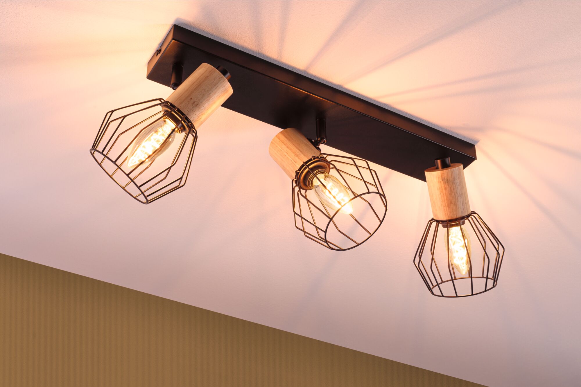 Spot plafond avec trois cages métalliques noires et détails en bois, lumière blanc chaud pour salon