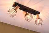 Deckenstrahler mit drei schwarzen Metallgittern und Holzdetails, warmweißes Licht für Wohnraumbeleuchtung